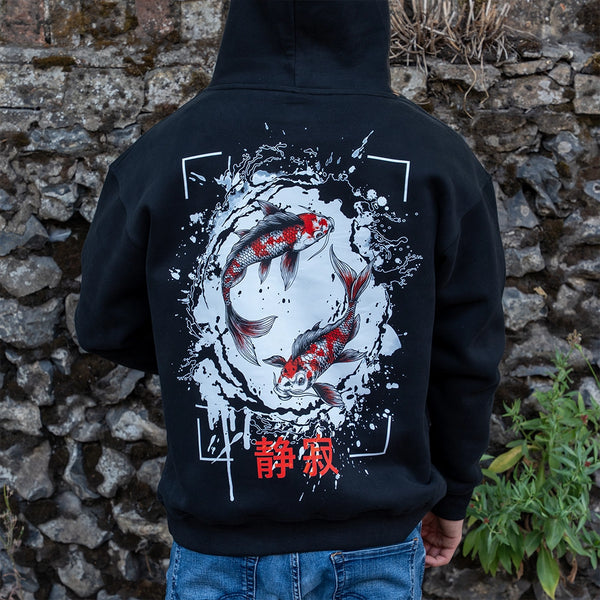 ArcaLoot Serenity black hoodie with Japanese koi fish back design, worn by a model against a cobblestone wall.