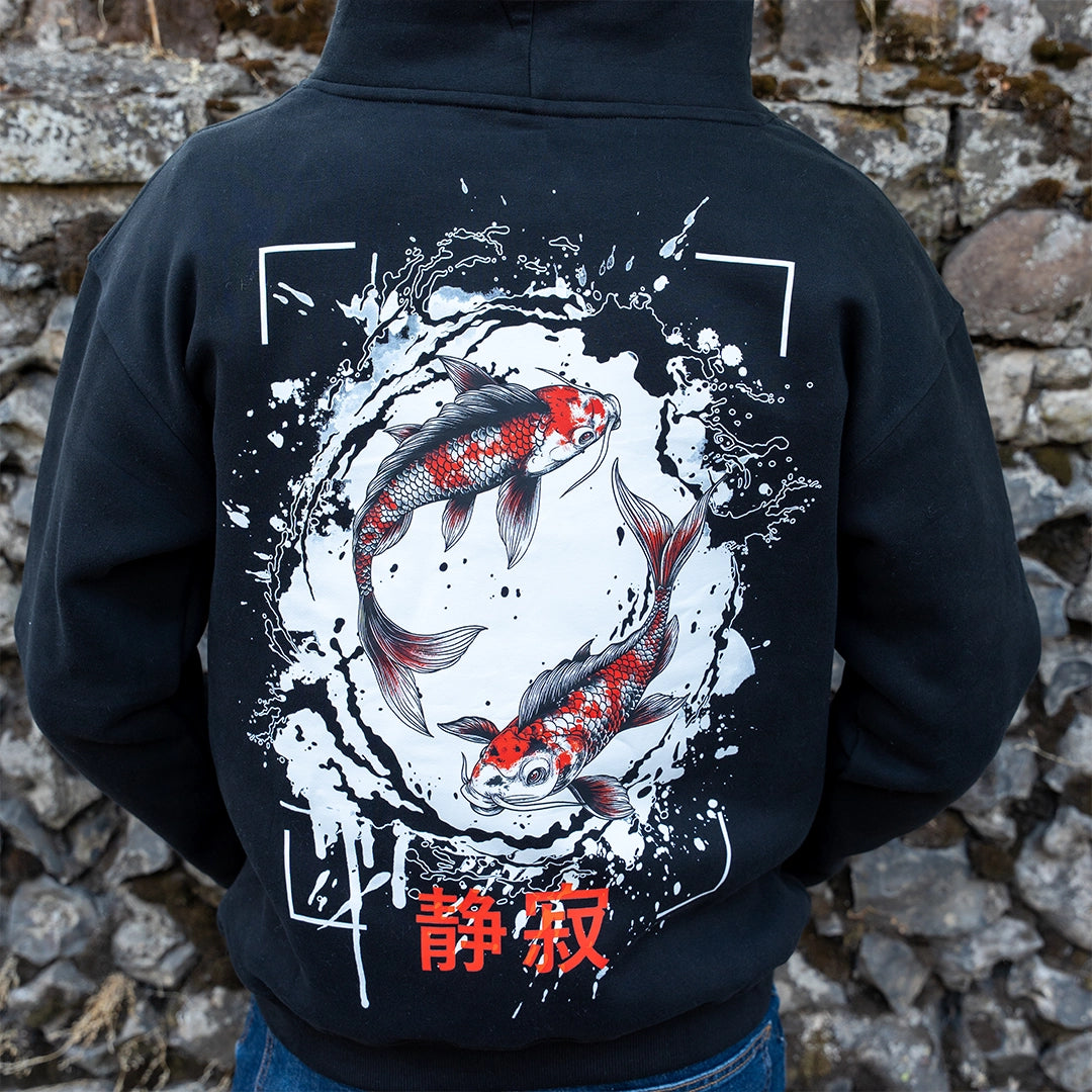 ArcaLoot Serenity black hoodie with Japanese koi fish back design, worn by a model against a cobblestone wall.