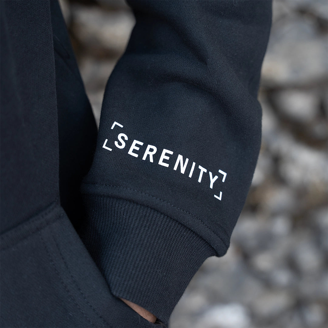 ArcaLoot Serenity black hoodie sleeve with English Serenity logo, worn against a cobblestone wall.