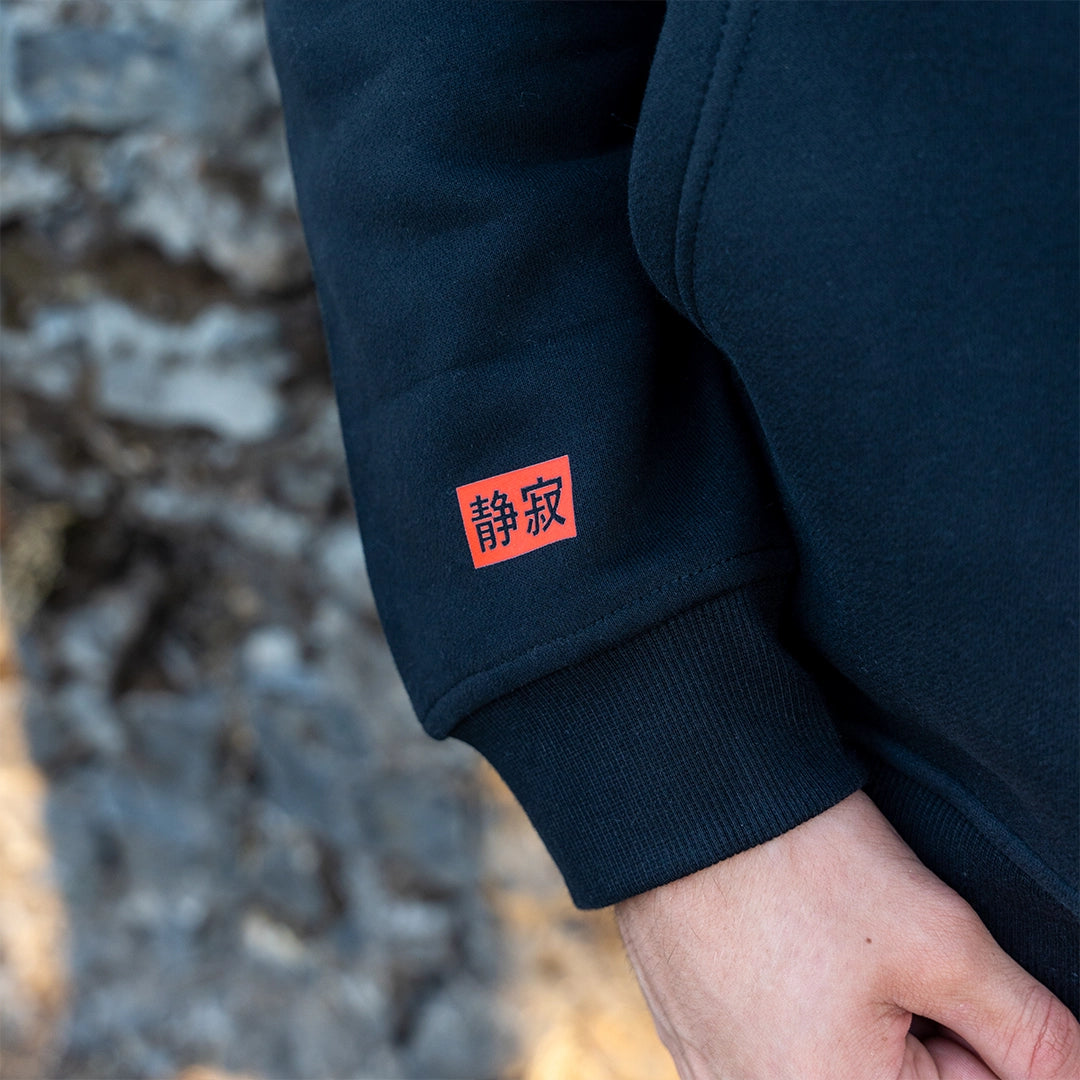 ArcaLoot Serenity black hoodie sleeve with Japanese Serenity logo, worn against a cobblestone wall.
