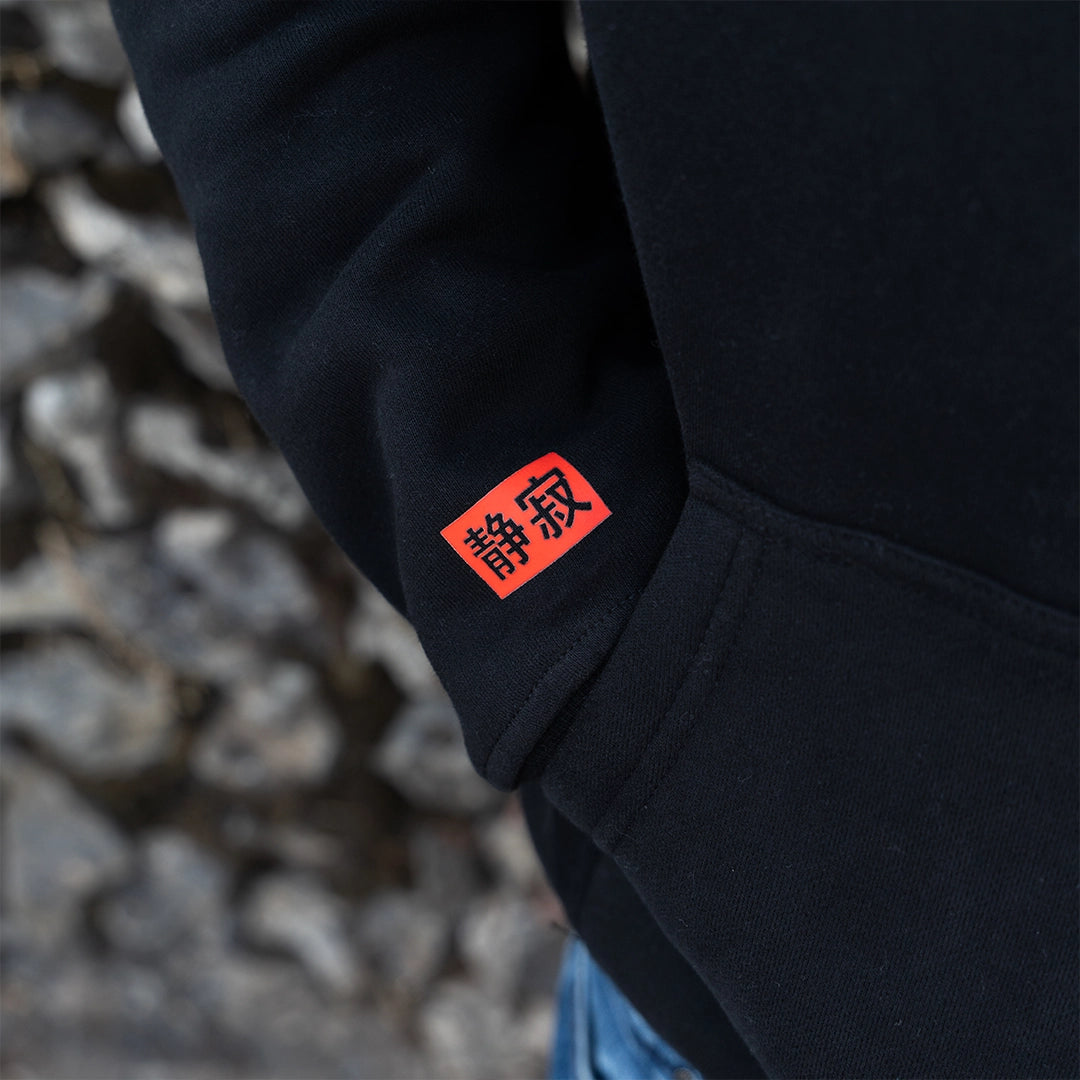 ArcaLoot Serenity black hoodie sleeve with Japanese Serenity logo, worn against a cobblestone wall.