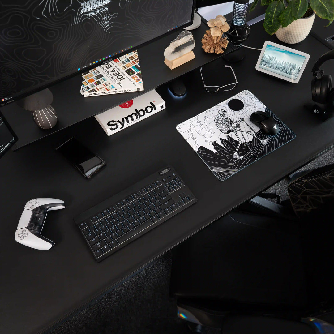 Small ArcaLoot gaming mousepad with a Skeleton figure hiking against a mountain landscape on a black gaming setup. Bare Boned Expedition. 