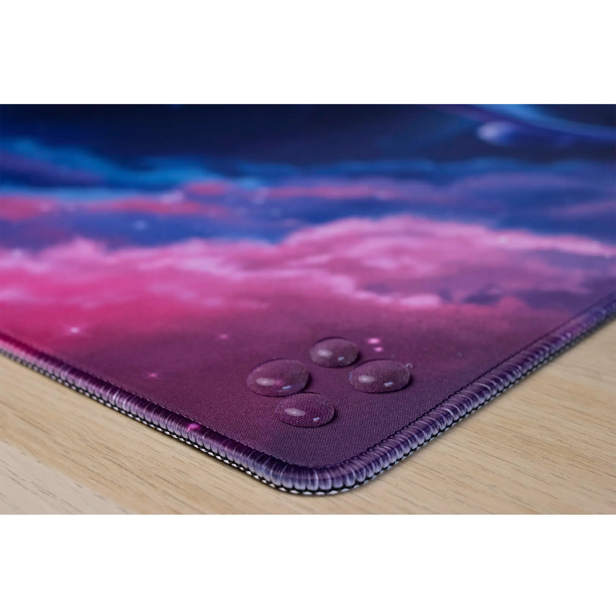 Clear water droplets on an ArcaLoot gaming mousepad featuring stitched edges. Cosmic Cetacean.