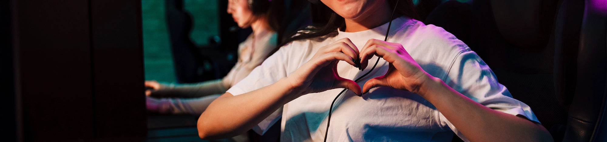 Person sitting with hands forming a heart shape in a dimly lit room.
