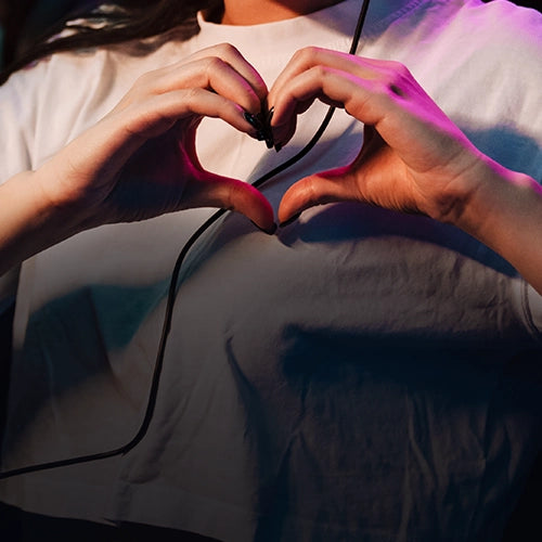 Person making a heart shape with their hands, wearing a white shirt.